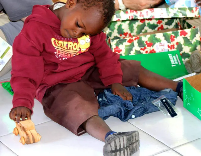 Boy lifting toy car with other children playing with toy cars around him.